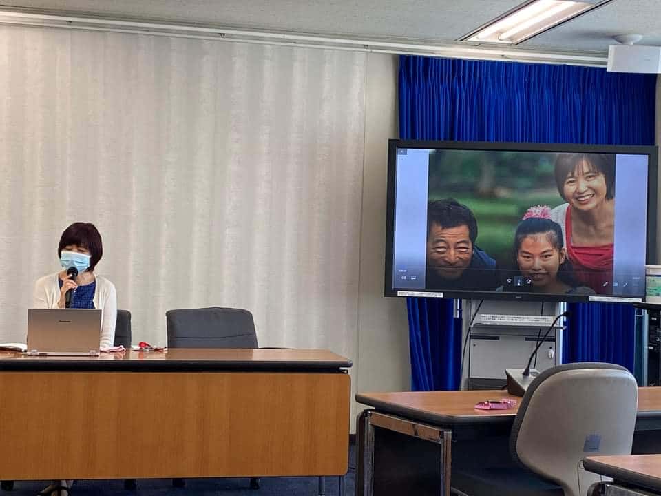 Junko’s press conference 2022 Woman speaking with microphone and tv with pictures is on in the background